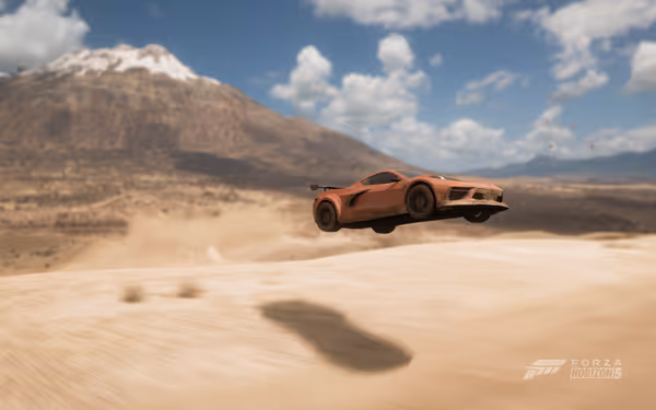 A sports car is airborne over a sandy desert landscape, with mountains and a clear sky in the background.