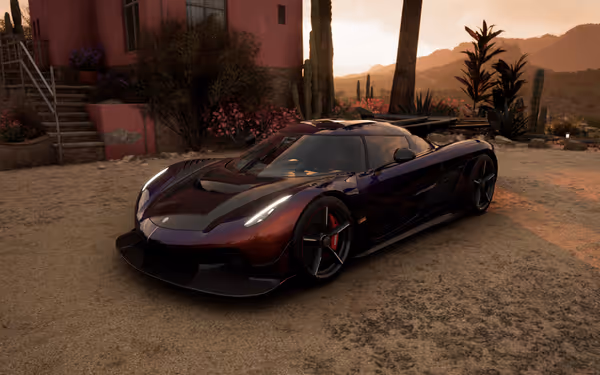 Dark violet sports car in front of pink house, surrounded by cacti and desert plants