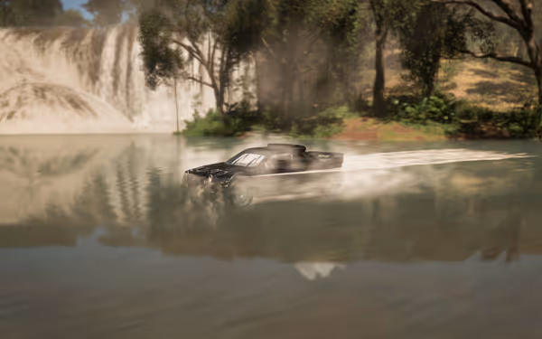 A black rally car speeds across shallow water, leaving a trail, with a waterfall behind.