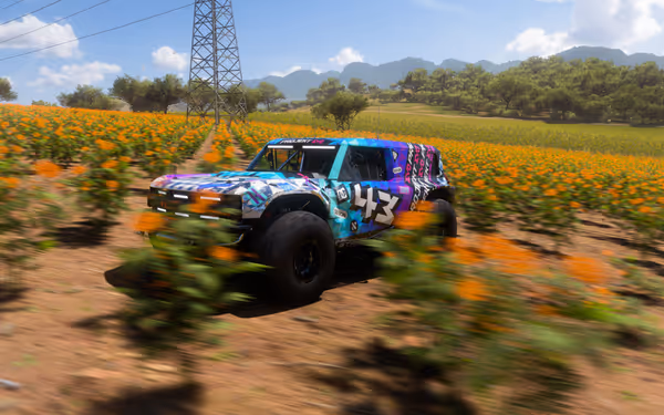 A colorful off-road vehicle speeds through a field of orange flowers with distant hills.