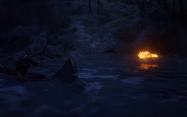 A person rows a wooden boat across the water beside a blazing campfire on the riverbank.