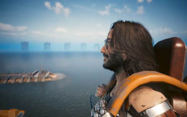 A man with long hair, sunglasses, and a cybernetic arm smiles while overlooking the ocean.