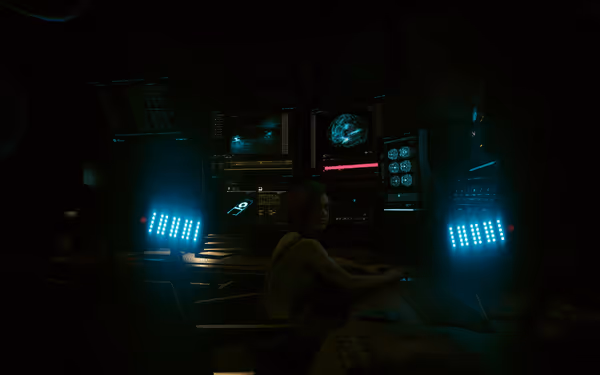 A woman sits at a futuristic computer setup with glowing screens and blue lights