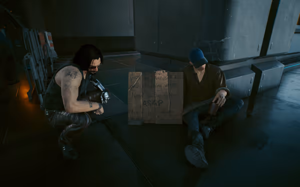 A man with a cybernetic arm crouches beside a homeless person holding a sign