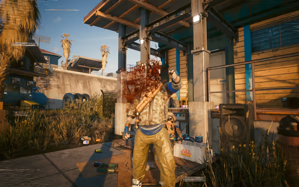 A man in tactical clothing stands headless and bloody in front of a small building.