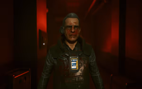 A man covered in blood  in police gear stands under red lights, wearing glasses and headset.