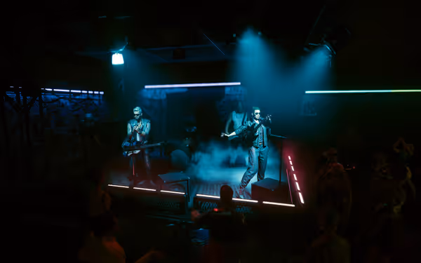 Band performs on neon-lit stage with guitars, smoke effects, and cheering crowd.