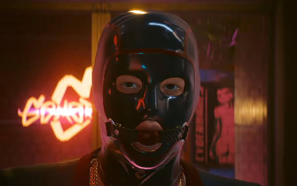 Person wearing a shiny black bondage hood with ball gag stares into camera under neon lights.
