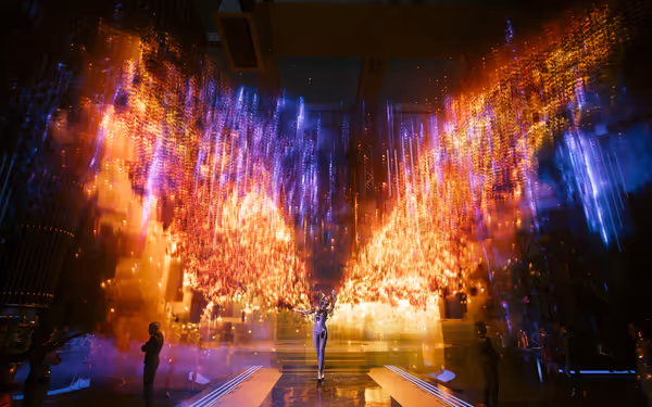 A performer in a sleek bodysuit stands beneath vivid holographic wings of light.