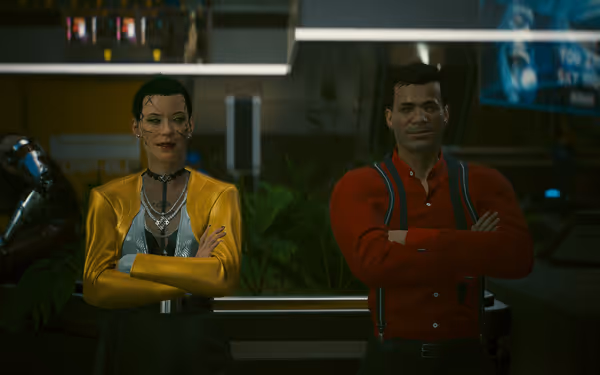 A woman in a yellow jacket and man in red shirt stand confidently arms-crossed.
