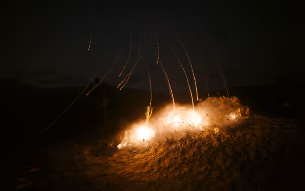 Multiple explosions erupt on a hillside at night with debris and smoke filling the air.