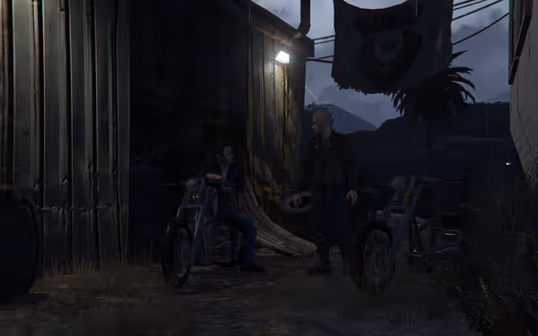 Two bikers talk outside a rundown building at night, beside their parked choppers.