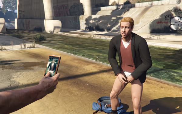 A man in underwear looks embarrassed as another photographs him with a smartphone.