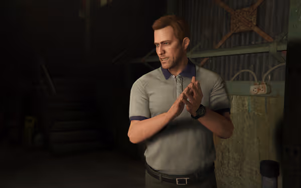 A man in a light grey polo shirt stands in an industrial room, clapping his hands.