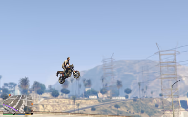 Person performing motorcycle wheelie jump against clear sky with power lines and city backdrop.