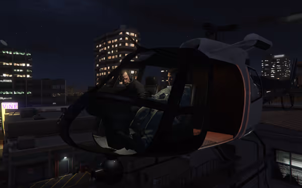 Two people sit inside a police helicopter above a city at night, surrounded by lit buildings.