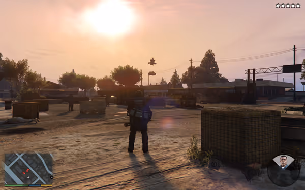 An armored figure stands in a dusty, open area with military obstacles and a setting sun.