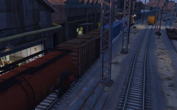 Several freight train cars are parked beside an industrial warehouse along multiple railway tracks.