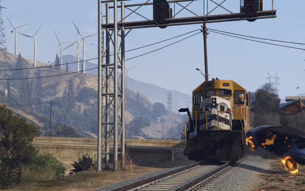 A yellow locomotive approaches on railroad tracks amid power lines and wind turbines.