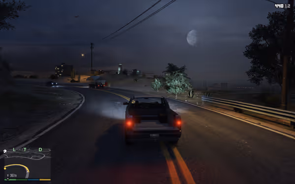 A pickup truck drives along a winding road at night under a half-moon, city lights visible.
