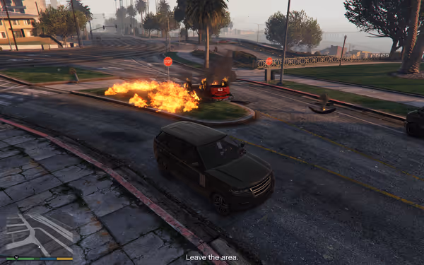 A dark SUV sits on a street as a fiery explosion burns near buildings and palm trees.