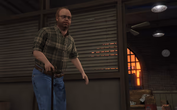 A man in glasses and a plaid shirt stands indoors holding a cane.