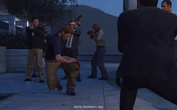 Several armed men stand on a sidewalk, one crouching clutching an injured, bleeding leg.