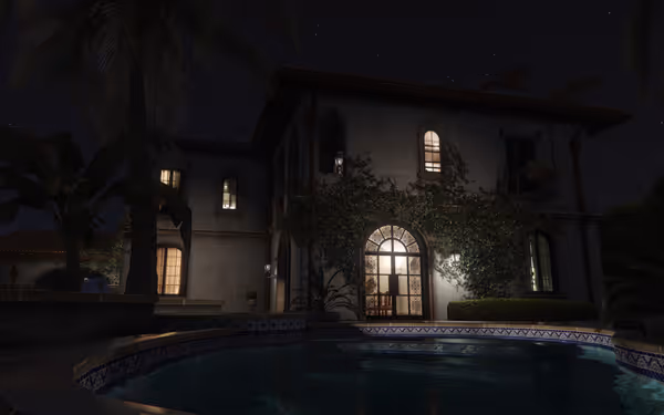 A large house with ivy-covered walls and lit windows sits next to a pool at night.