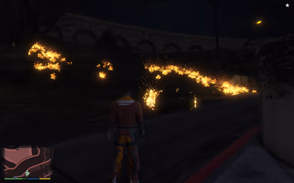 A person stands watching a car engulfed in flames on a dark hillside.