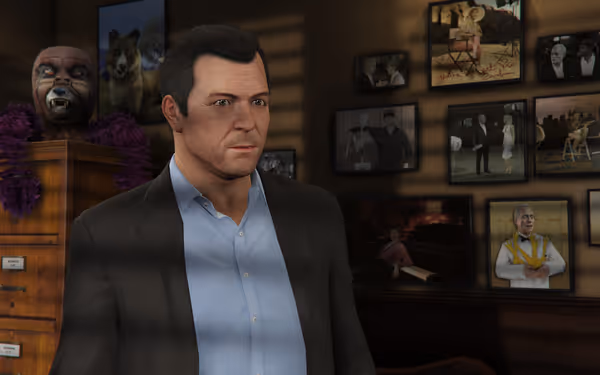 A man in a suit stands indoors with framed photos and decorations on the wall behind him.