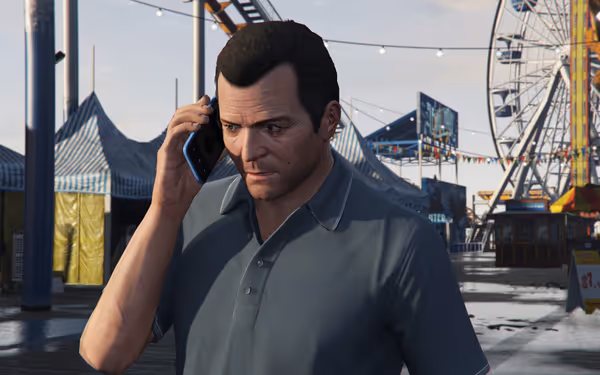 A man in a blue shirt talks on a phone at an amusement park pier.