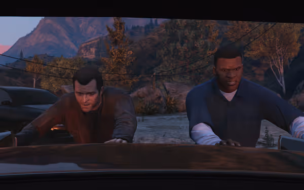 Two men push a vehicle from behind, with mountains and trees in the background.