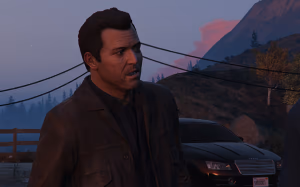 A man in a dark jacket stands beside a black car in front of hills and power lines.