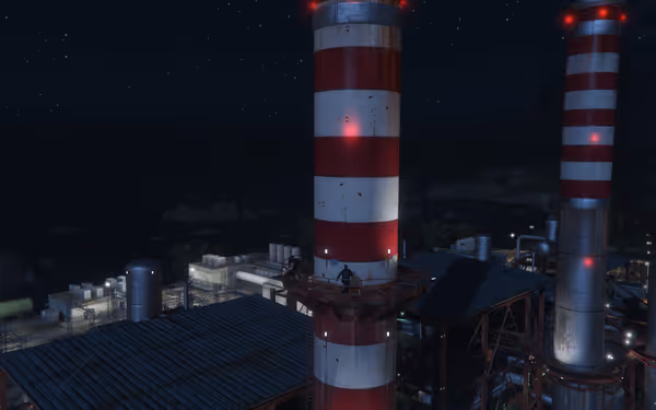 A person is standing on the railing of a red and white striped industrial chimney at night.