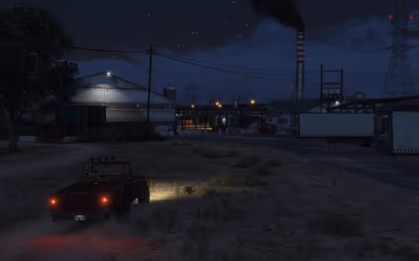 A red off-road vehicle drives toward an industrial area at night with smoke rising.