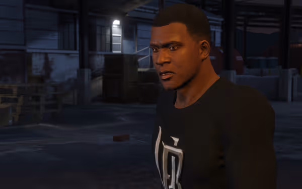 A close-up of a man with short hair, wearing a black shirt in a dimly lit warehouse setting.