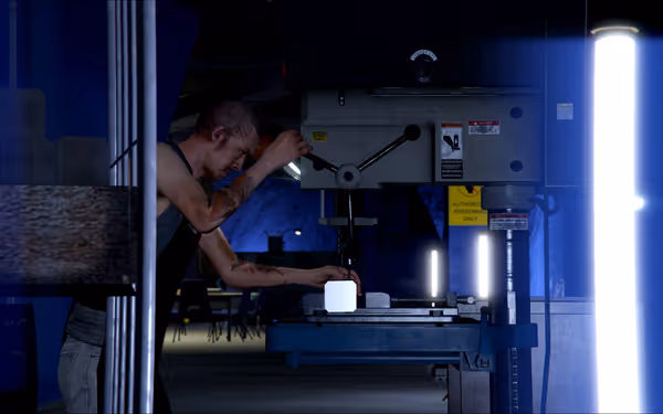 A person with tattoos operates heavy machinery in an industrial, blue-lit indoor space.