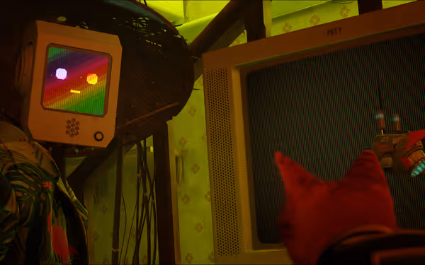 A robot with a rainbow screen face watches a monitor as a cat points.